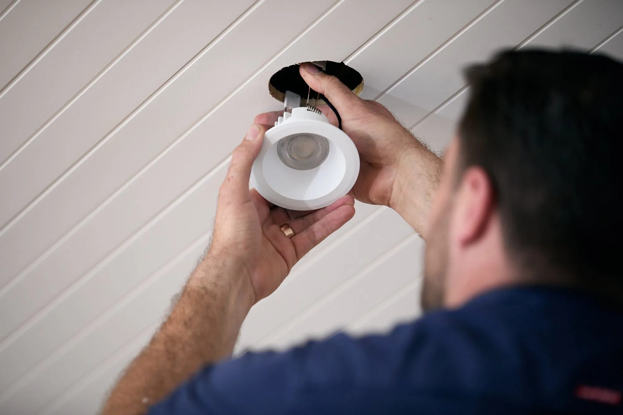Anthony Kitson fitting an LED downlight, seen over his shoulder