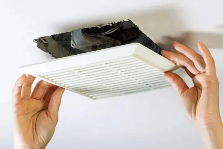 Hands fitting a ceiling exhaust fan grille