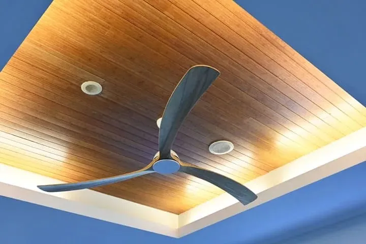 A three-blade ceiling fan on a timber ceiling with downlights