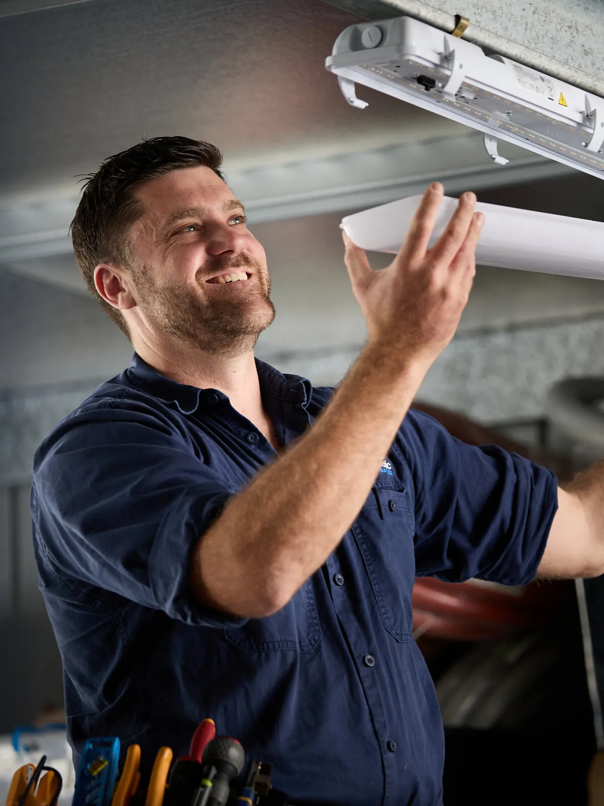 Kitson electrician fitting an LED batten light in a warehouse
