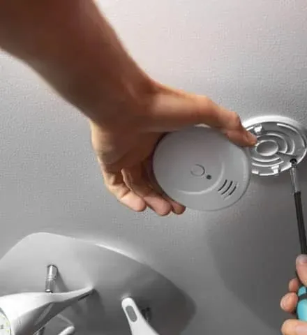 A smoke alarm being fixed to its ceiling mount