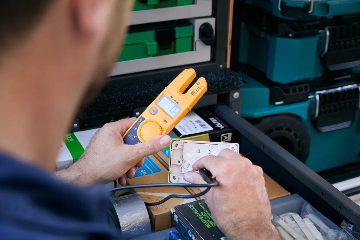An electrician testing a power point with a clamp meter