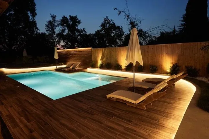 A backyard pool and timber deck lit up at night